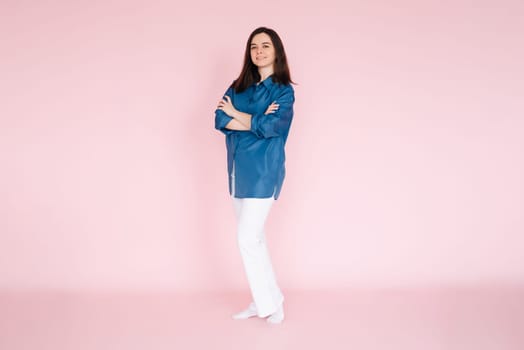 Portrait of professional businesswoman in smart casual attire standing confidently with folded hands, isolated on a pink background