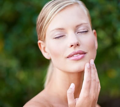 Skincare, beauty and a woman touching face in a garden nature or backyard. Content, wellness and a young lady feeling skin for moisturizing, satisfaction or wellbeing glow from a spa treatment