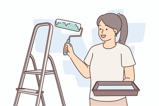 Woman molar with roller for painting walls stands near ladder making repairs in apartment