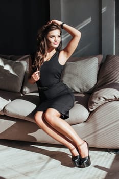 Portrait of a sexy brunette in a black dress on a dark background. girl takes off her dress slowly in the bedroom