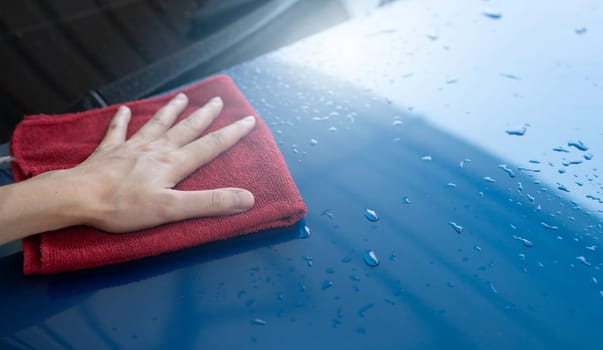 Car wash service. Man hand holding red microfiber cloth polish blue car and water drop after cleaning. Auto care service business concept. Man cleaning and detailing luxury car with microfiber cloth.