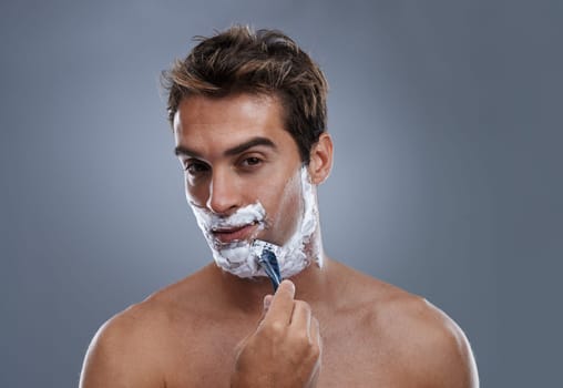 Getting the closest shave ever. Head and shoulders studio shot of a young man shaving.