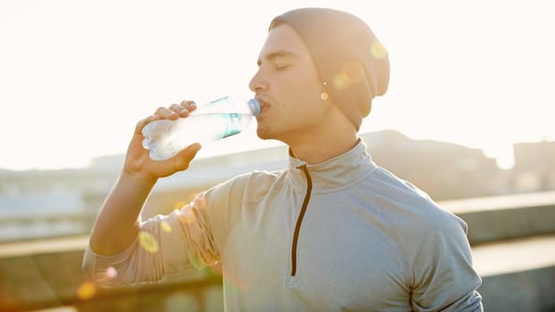 Thirst quenching. a young male jogger drinking water while out for a run in the city.
