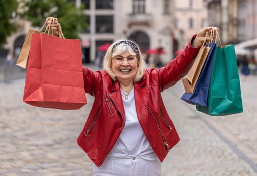 Happy senior woman shopaholic consumer after shopping sale with full bags walking in city street