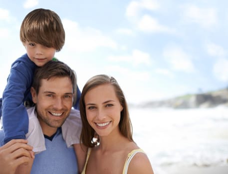 Happy family, portrait and blue sky at beach on travel, holiday or vacation in summer with a smile. Man, woman and child together on adventure or quality time at sea with happiness, love and care