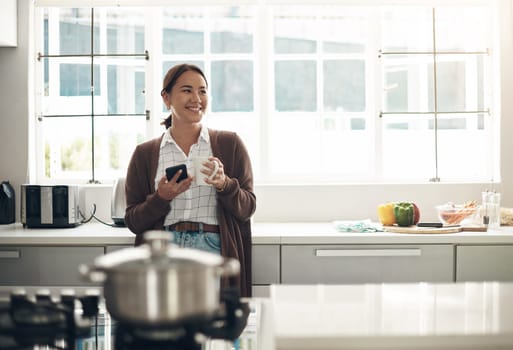 Enjoying a little caffeine boost with her connection. a young woman using a cellphone while drinking coffee in the kitchen at home.