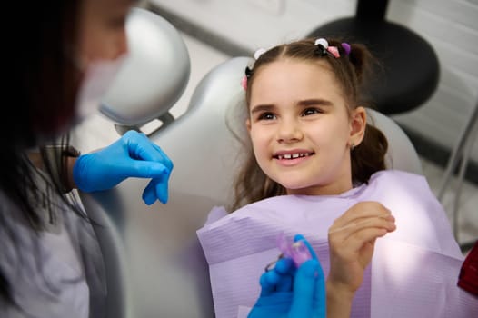 Little child girl in dentist's chair, smiles to her doctor during regular dental check-up in pediatric dentistry clinic