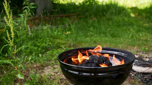 Black round Barbecue Grill with Fire on Open Air with green grass. Fire Flame. Prepairing charcoal for the grilling bbq outdoors.