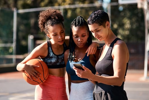 This is how we played today. a diverse group of sportswomen standing together after playing basketball and looking at a cellphone.