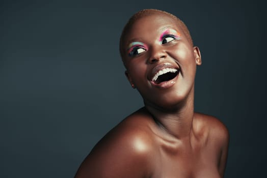 A happy woman is a beautiful woman. a beautiful woman wearing colorful eyeshadow while posing against a grey background.