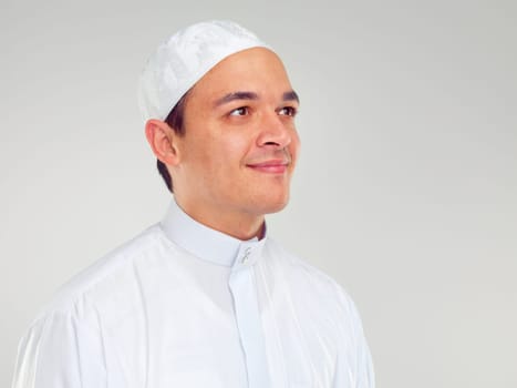Islam, culture and portrait of muslim man with smile on face in ramadan isolated on grey background. Youth, spiritual wellness and religion, happy Islamic scholar in white from Saudi Arabia in studio