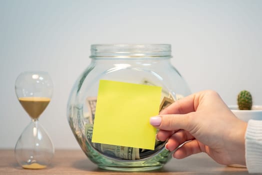 Female hand putting empty sticky note to the glass bank