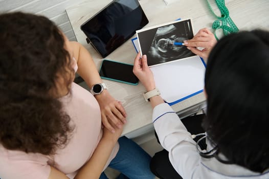 Doctor obstetrician gynecologist holds ultrasound scan, explains to pregnant woman the development of her child in womb