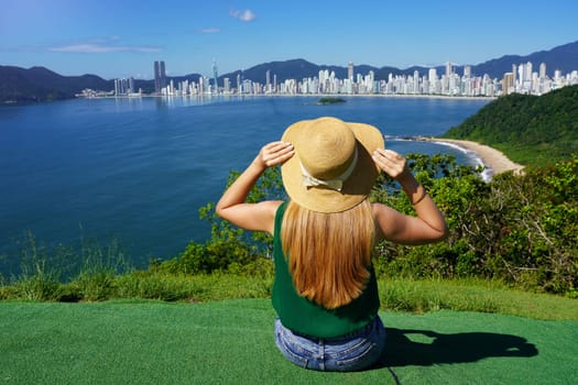 Holidays in Brazil. Traveler girl sitting on viewpoint enjoying Balneario Camboriu skyline on Atlantic Ocean, Brazil.