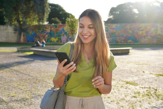 Brazilian girl using mobile phone outdoor with colorful background on sunset