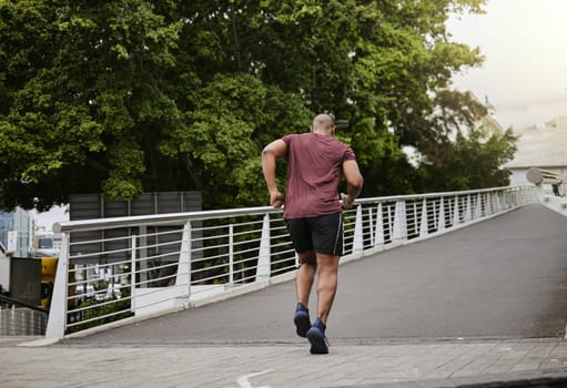 Fitness, running and man on a bridge for training, wellness and cardio in a city, cardio and energy. Sports, runner and male exercise on a highway for run, challenge and body performance goals