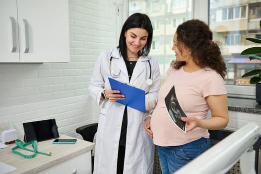 Smiling pregnant woman visiting doctor gynecologist obstetrician in gynecological clinic, during regular medical checkup