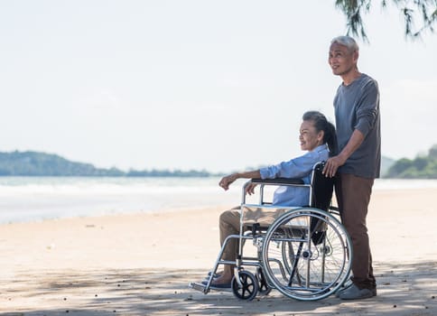 back elderly woman disabled sitting in wheelchair and husband is a wheelchair user on the beach