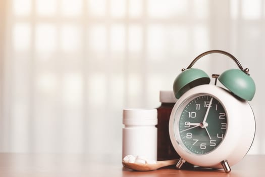An alarm clock with pills on the wooden spoon and medicine bottles on the table