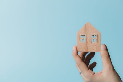 Hand holding a wooden house model on blue background