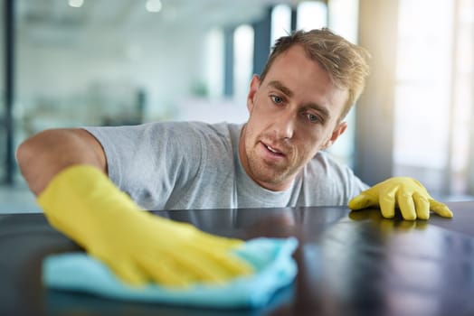 Man with gloves, office cleaning service and janitor dusting dirt for health and hygiene in workplace. Professional cleaner wiping table in workspace, maintenance and disinfectant on cloth for germs.