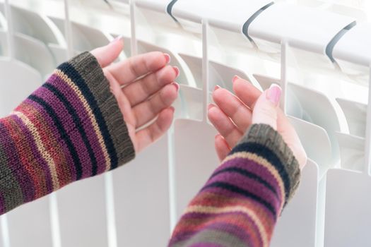 Girl warms up the frozen hands above hot radiator, close up view