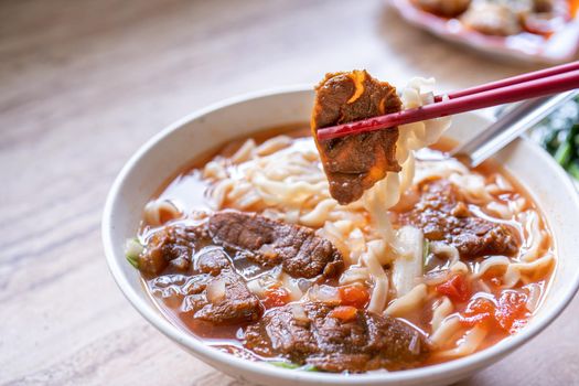 Beef noodle - Taiwan ramen meal with tomato sauce broth in bowl on bright wooden table, famous chinese style food, close up, top view, copy space