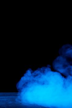 Conceptual image of blue smoke isolated on dark black background and wooden table.