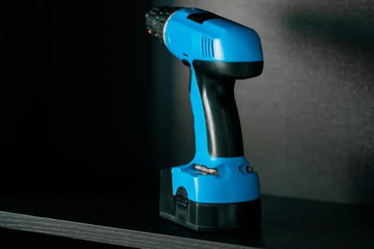 Cordless screwdriver or blue cordless drill stands on the shelf