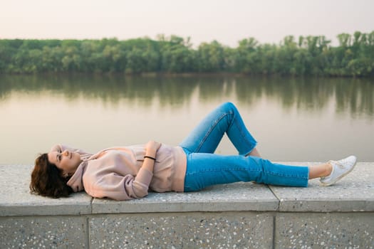 Woman lying down on embankment by lake or river at city park - dreamer and relax concept