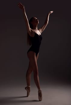 Ballet, woman and dancer with routine, fitness and training for performance on a dark studio background. Female performer, lady and ballerina with wellness, focus and commitment for art or creativity