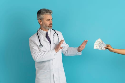 Mature doctor refusing to take bribe from patient on blue