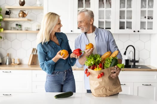 Happy Senior Couple Unpacking Paper Bag With Fresh Vegetables After Grocery Shopping