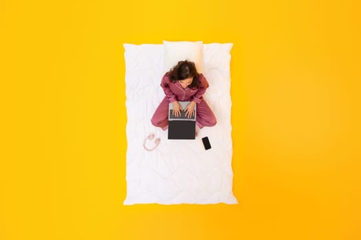 Woman In Sleepwear Multitasking On Laptop, Yellow Background, Above View