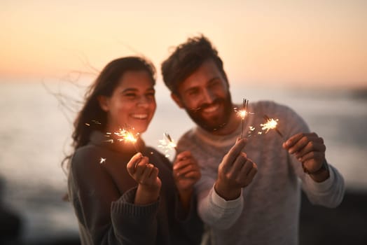 Happy, beach and couple with sparklers for celebration and party with sparks on romantic date. Love, sunset and excited man and woman with fireworks for honeymoon on holiday, weekend and vacation.