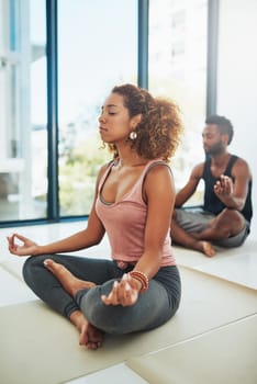 Meditation is getting to know how your mind works. Shot of two people doing yoga together in a studio.