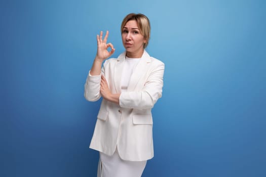 confident slim blondie young business woman in a white jacket on a blue background with copy space
