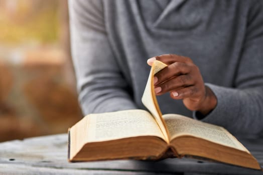 Hands, spiritual and a man reading the bible at a table outdoor in the park for faith or belief in god. Book, story and religion with a male christian sitting in the garden for learning or worship