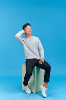 Casual young man sitting on a mint column isolated on blue background