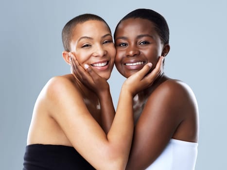 We are more alike than you think. Portrait shot of two beautiful young women holding each others face while standing against a grey background.