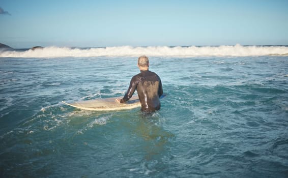 Surfer and man in water watching wave for high tide while holding surfboard at sunny USA beach. Retirement person enjoying surfing sport leisure in California waiting for ocean level to rise.