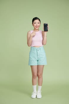 Young Asian woman holding phone in hand and pointing at it with playful expression