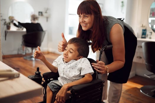 Hair salon, hairdresser and child in wheelchair with thumbs up after haircut. Hairdressing, barber and haircare for kid with disability. Support of accessibility, smile and thank you from happy boy