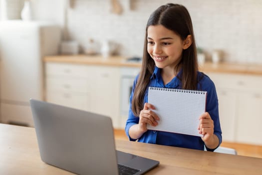 Schoolgirl Showing Workbook To Laptop During Distance Lesson At Home