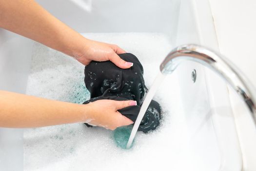 Female hands washing black clothes in basin