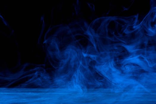 Conceptual image of blue smoke isolated on dark black background and wooden table.