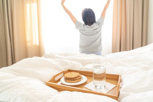 Tray with diet breakfast on a bed with woman stretching on background