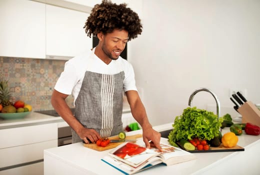 Smiling African American Guy Reading Paper Culinary Book In Kitchen