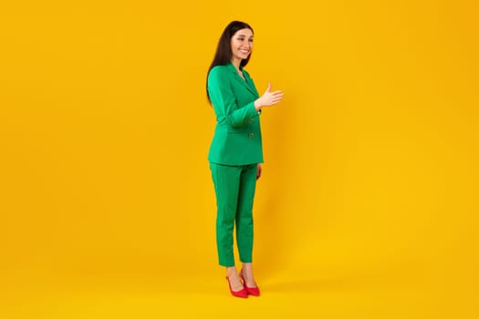 Young stylish woman stretching hand for handshake, greeting and smiling, standing over yellow background, full length