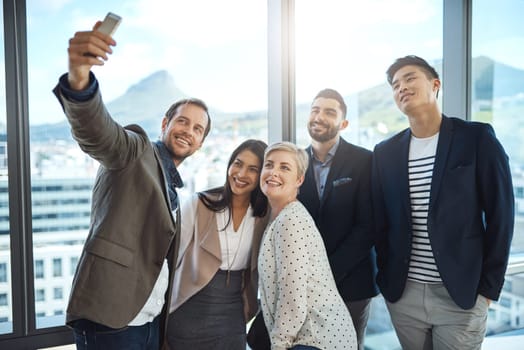 Capturing every moment of our success. a group of businesspeople taking a selfie together in an office.